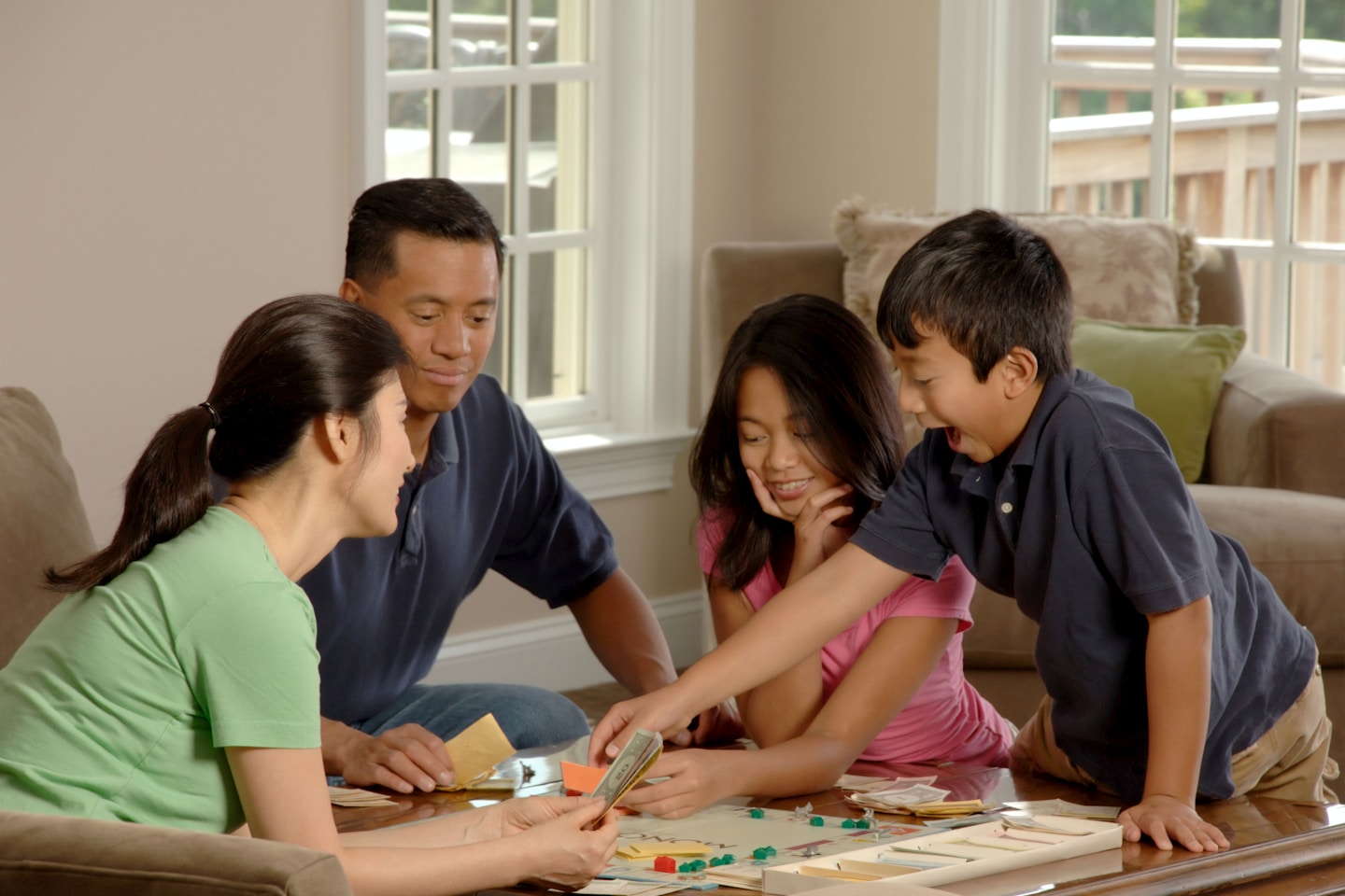 Family Playing A Board Game. An Asian family (adult male and female and two adolescents, male and female) sitting around a coffee table playing a board game. Photographer Bill Branson