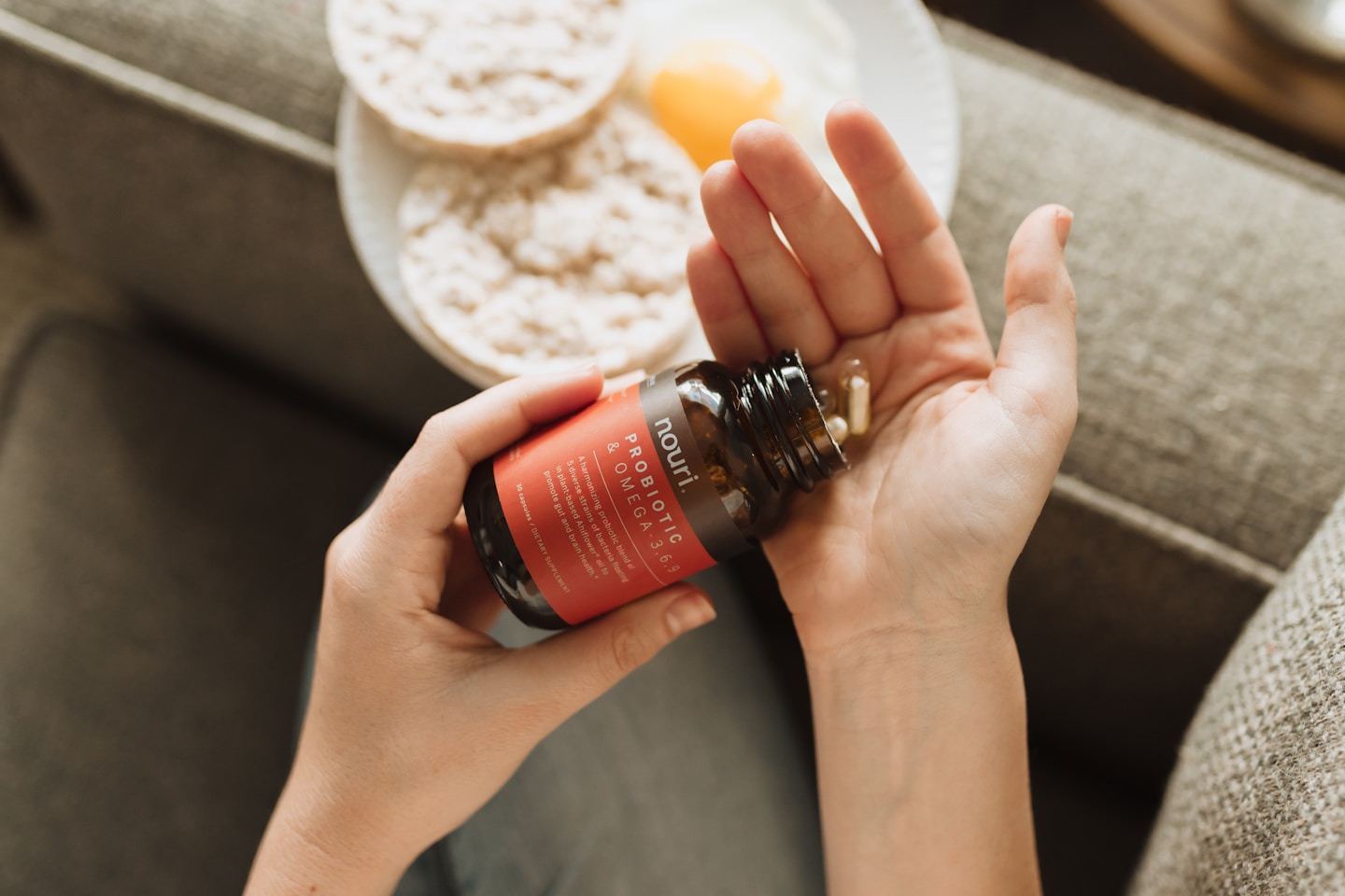 Woman taking supplements in the morning. A plate of breakfast remains in the background. Woman puts probiotic capsule pills into her hand for her morning health care routine.