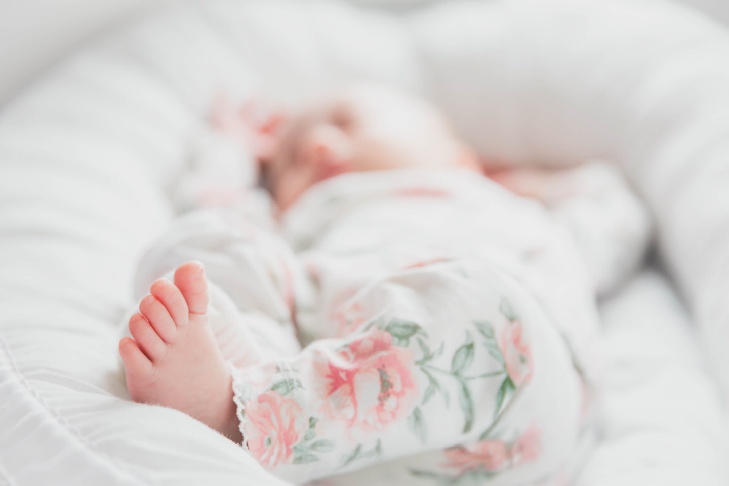 baby in white and red floral onesie lying on bed
