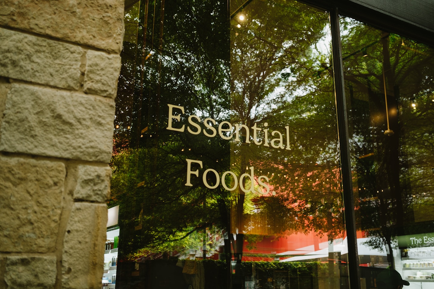 Essential foods sign on a glass window with tree reflections.