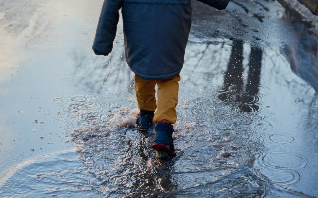 Enfant en manteau et bottines qui marche dans une flaque un jour de pluie