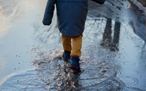 Enfant en manteau et bottines qui marche dans une flaque un jour de pluie